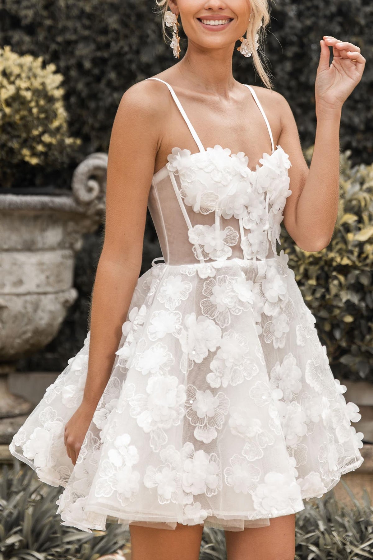 Close up image of white mini dress featuring hand-sewn 3D flower appliques over flower lace, sheer corset bodice, layered tulle puffy skirt, thin shoulder straps