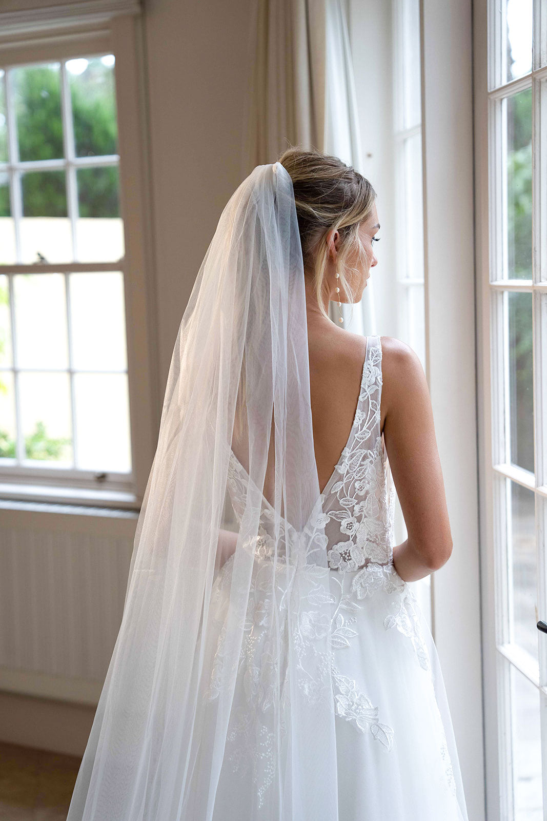 Open Back Design of Ivory White A-line Wedding Gown with V Neckline adorned with Lace Appliques, Sheer Bodice and Full Voluminous Layered Tulle Skirt worn with White Tulle Wedding Veil