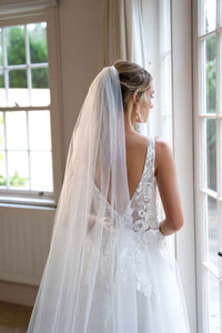 Open Back Design of Ivory White A-line Wedding Gown with V Neckline adorned with Lace Appliques, Sheer Bodice and Full Voluminous Layered Tulle Skirt worn with White Tulle Wedding Veil