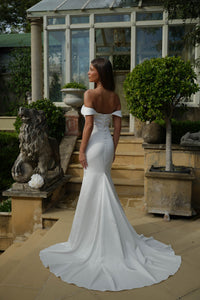 Woman in a white off-shoulder wedding dress standing in a garden setting.