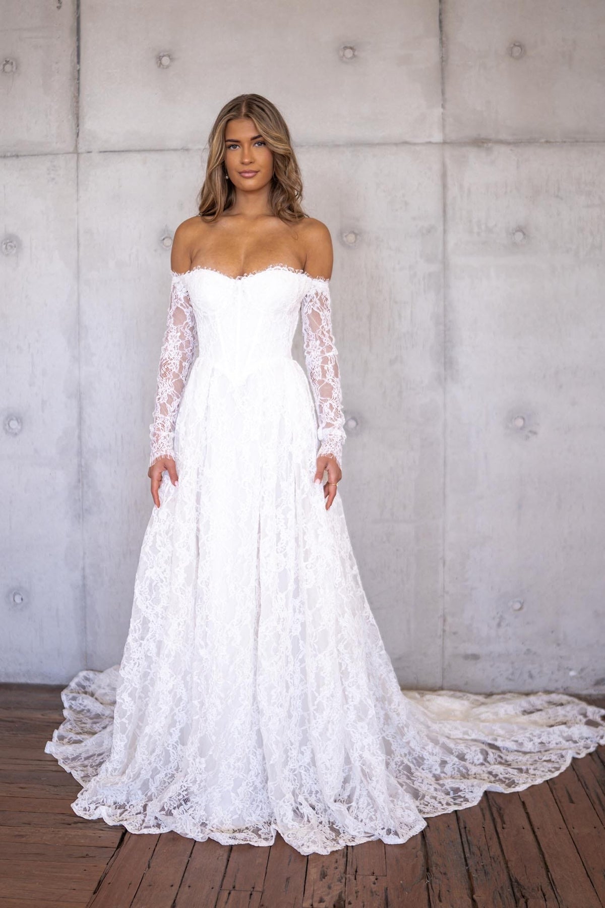 Ivory White Off The Shoulder Long Sleeve Lace Wedding Gown featuring Sweetheart Neckline with Lace Trimming Detail, Sheer Long Sleeves, Corset Bodice, Basque Waistline, Full A-line Skirt and Long Train.