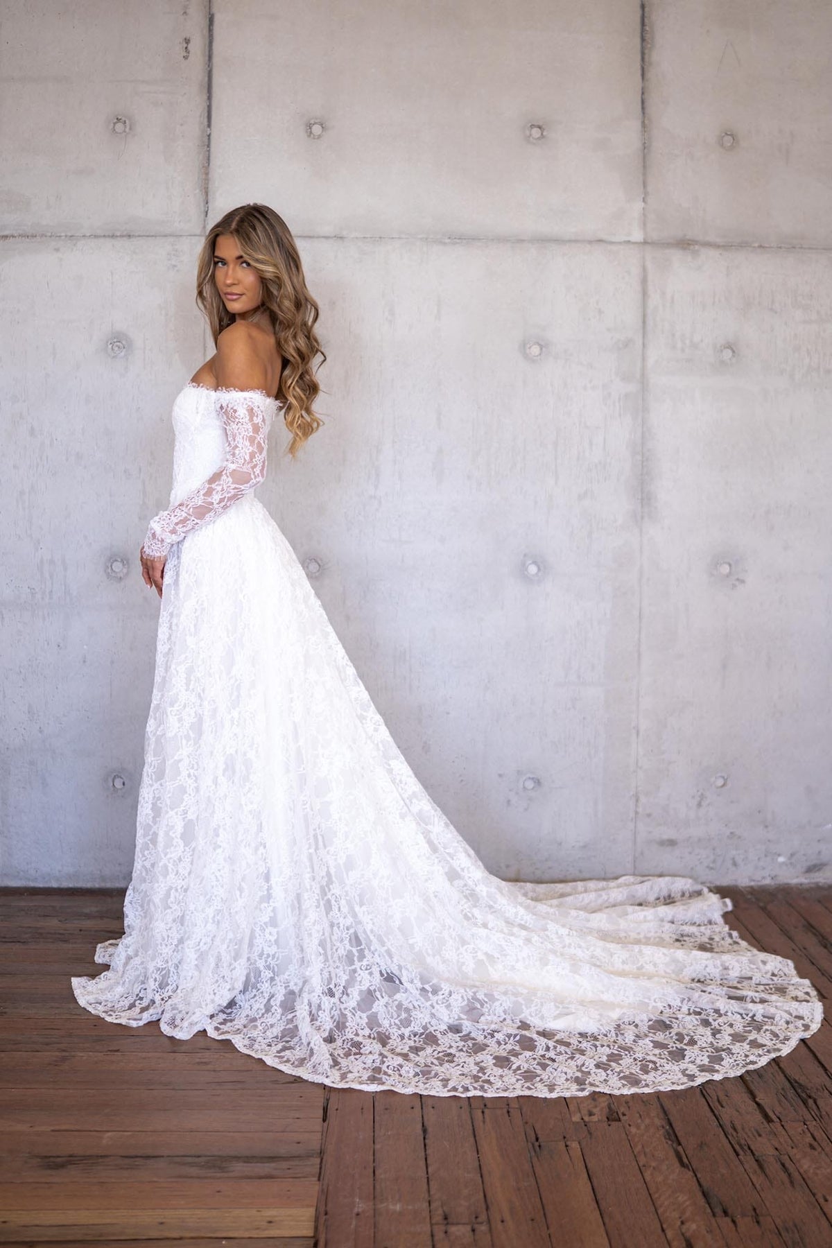 Side Image of Ivory White Off The Shoulder Long Sleeve Lace Wedding Gown featuring Sweetheart Neckline with Lace Trimming Detail, Sheer Long Sleeves, Corset Bodice, Basque Waistline, Full A-line Skirt and Long Train.
